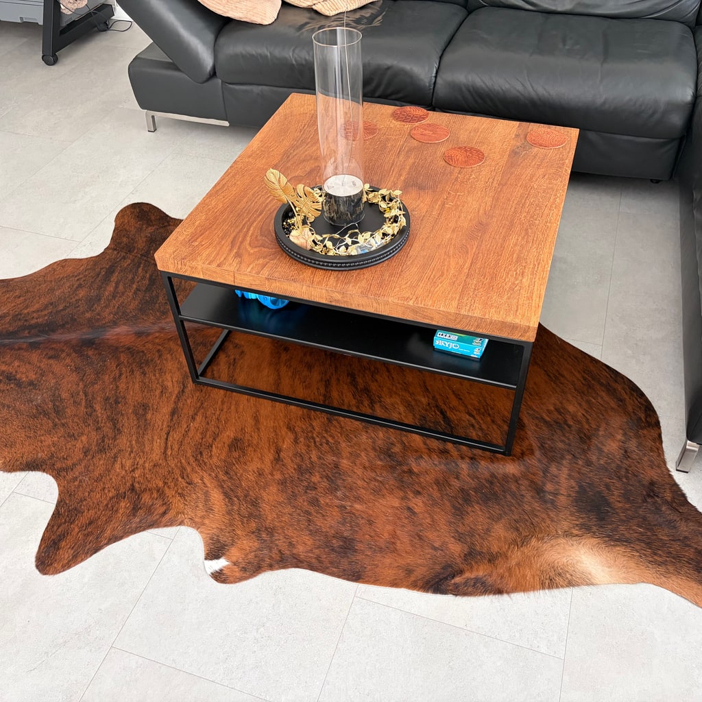 Bruin gemêleerde koeienhuid onder een salontafel in een woonkamer met een zwarte leren bank.