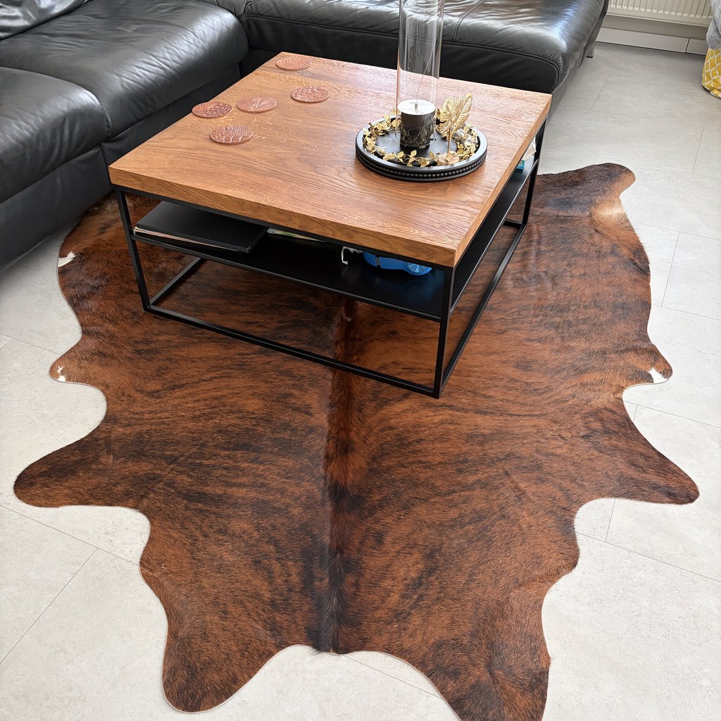 Bruin gemêleerde koeienhuid onder een salontafel in een woonkamer met een zwarte leren bank.