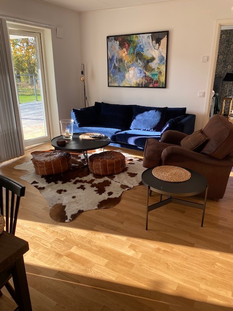 Bruin-witte koeienhuid onder een zwart rond salontafeltje en leren poefs, bij een blauwe bank op een houten vloer.