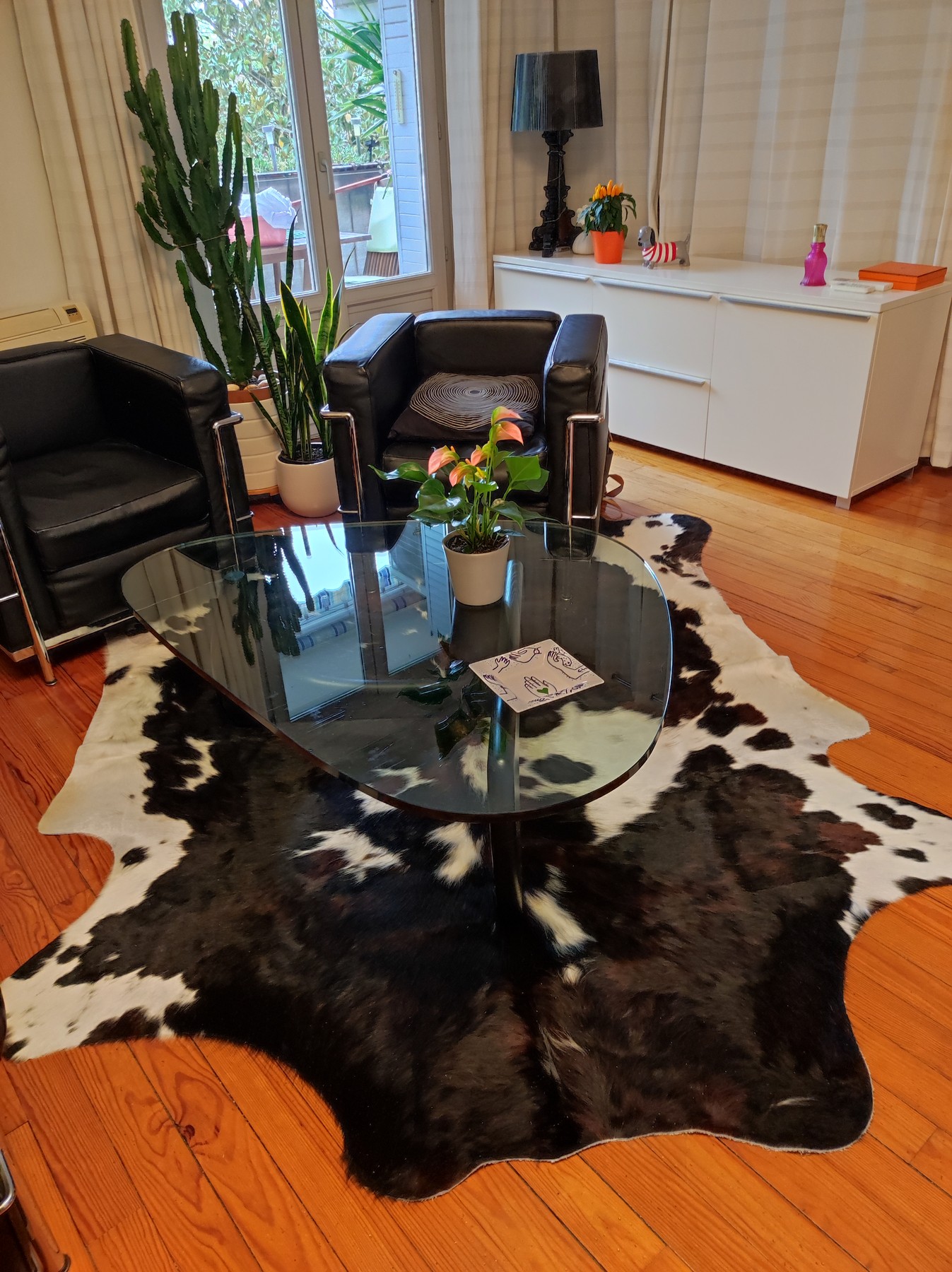 Bruin-witte koeienhuid onder een glazen salontafel bij zwarte leren zitmeubels