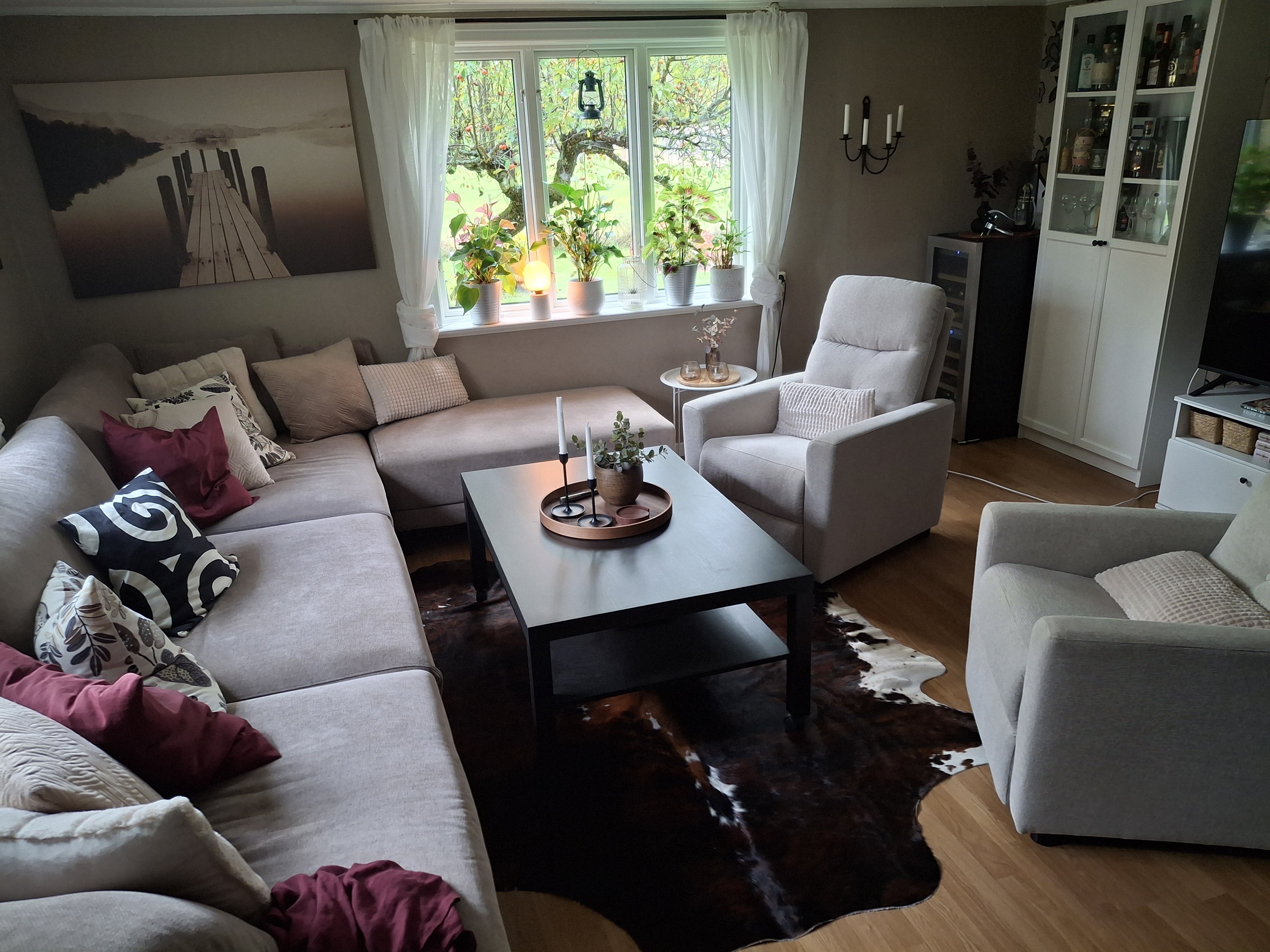 Bruin-witte koeienhuid onder een donkere salontafel, tussen een lichte hoekbank en fauteuils