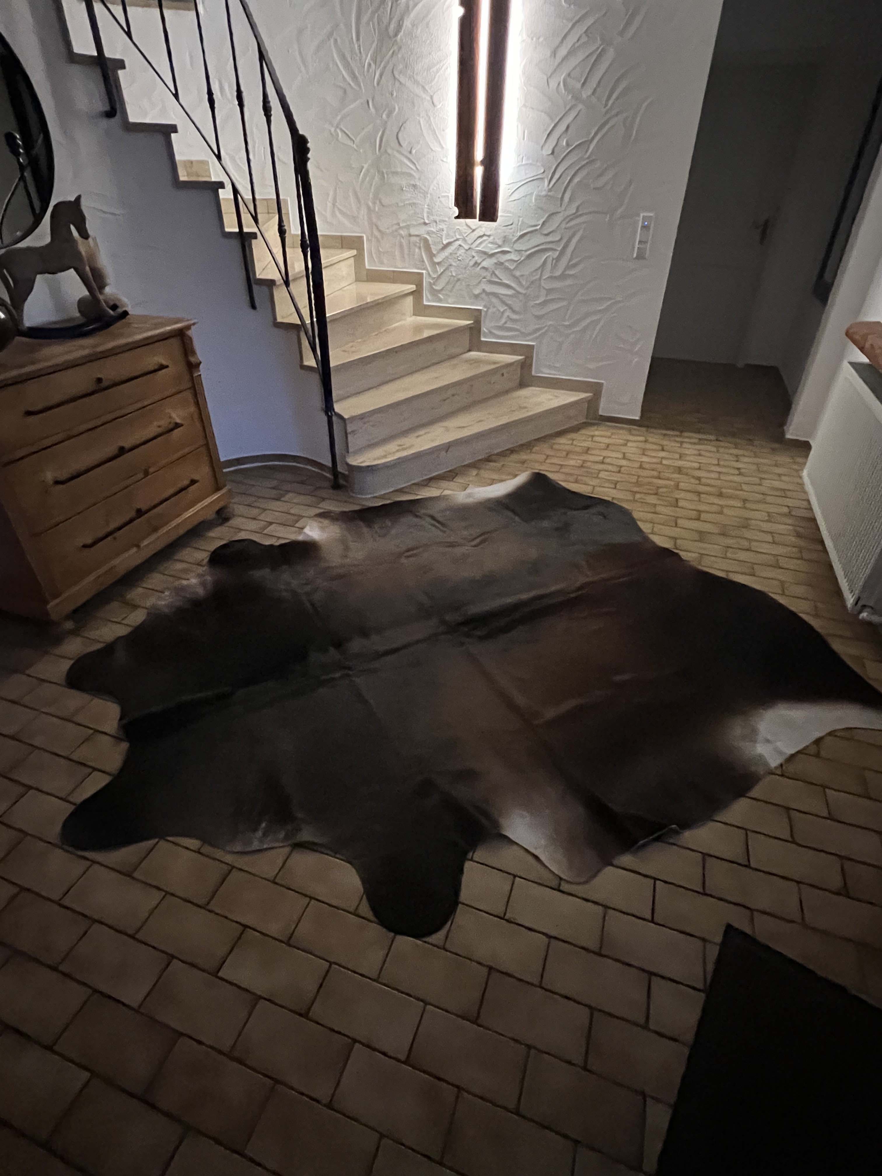 Donkere koeienhuid op een stenen vloer naast een lichte stenen trap en houten ladekast