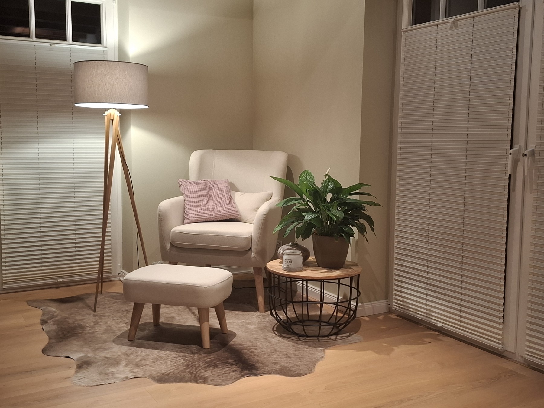 Grijsbruine koeienhuid onder een beige fauteuil met voetenbank, naast een staande lamp en bijzettafel