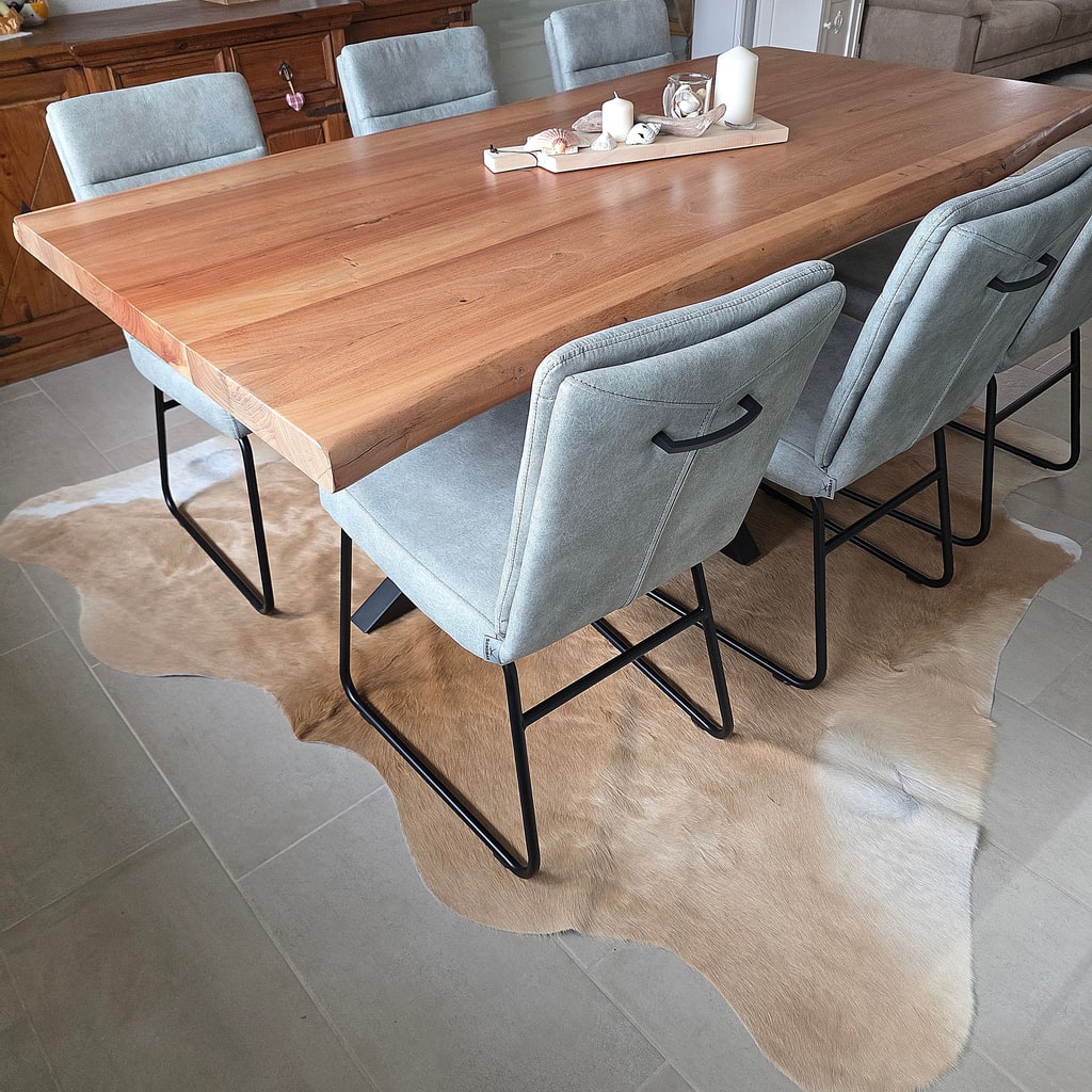 Lichtbruine koeienhuid onder een grote houten eettafel met grijze stoelen.